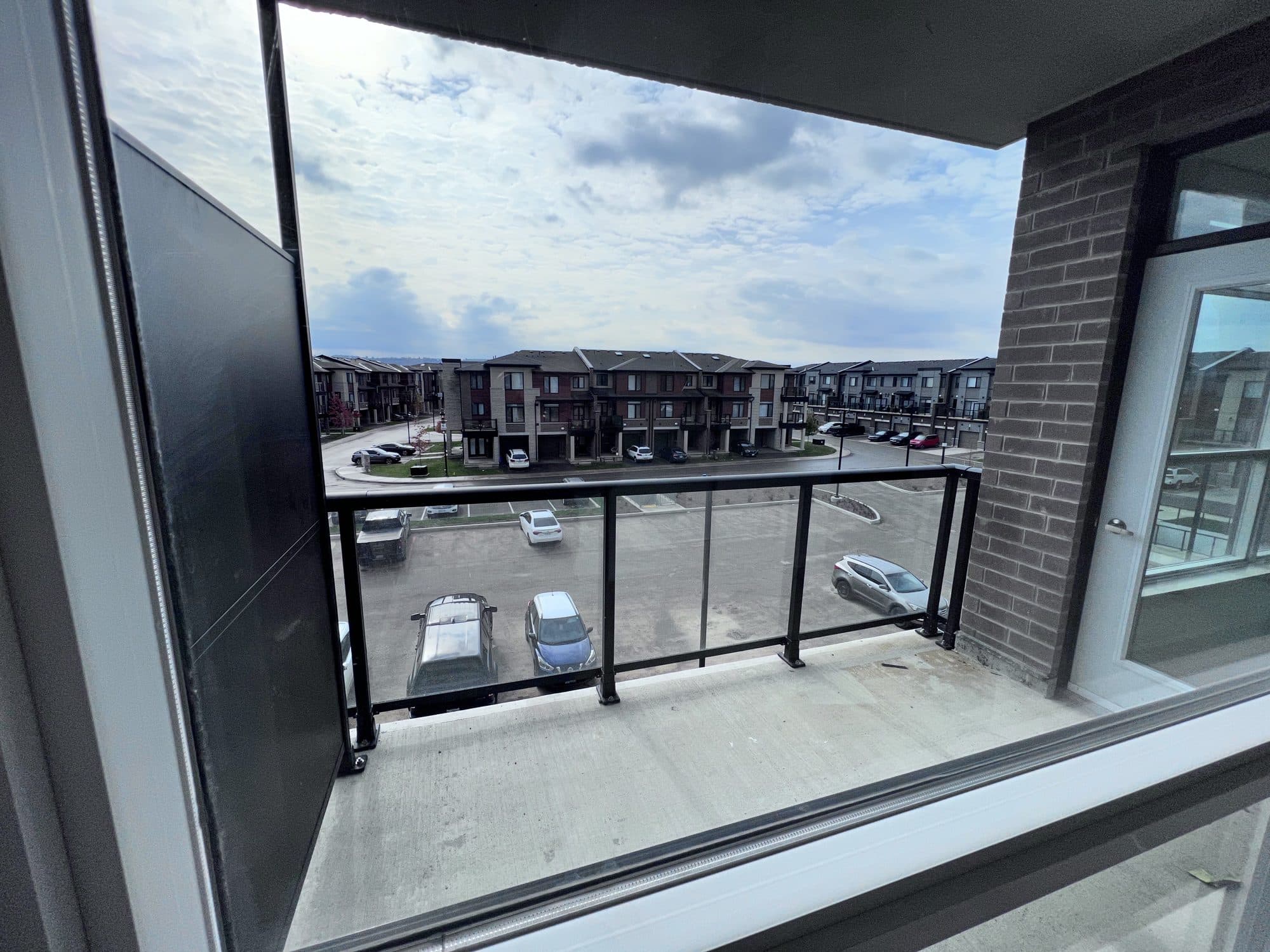 The view from a condominium balcony over a parking court and a long row of brick townhouses, under a bright part-clouded sky.